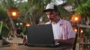 Freelancer deniz kenarında çalışıyor, doğanın tadını çıkarıyor. Odaklanmış adam gün batımlı plaj kafesinde dizüstü bilgisayar kullanıyor. Profesyoneller görevlerini tamamlar, okyanus kıyısında dinlenir. Dijital göçebe tipler, iş seyahatlerini yönetir. Yavaşla