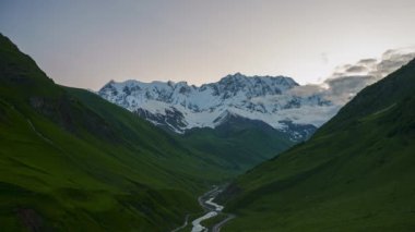 Gün doğumunda Shkhara zirvesinin zamanlaması. Kafkasya 'da karla kaplı dağlar. Akıntılı yeşil vadiler. Svaneti peyzaj dönüşümleri, geceden şafağa.