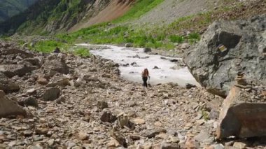 Nehir kenarındaki kayalık dağ arazisinde yürüyüş yapan bir kadın. Vahşi doğada maceralı bir seyahat. Temiz nehir havası. Tek başına gezen kadın zorlu yolları keşfeder. Açık hava macerası. Yavaşla