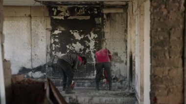2023-07-30 - Mariupol, Ukrayna. Koruyucu teçhizatlı işçiler yanan duvarları yıkıyor, savaştan zarar görmüş apartmanın zeminini matkap enkazı kullanarak yıkıyorlar. Yavaş çekim.