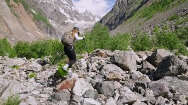 Kayalık yolda yürüyüş yapan bir kadın. Dişi sırt çantalı gezgin dağlarda yürümeyi sever. Yürüyüş direkleri olan turist kız milli parkta doğa keşfi yapıyor. Dağ tırmanışı macerası. Yavaş çekim.