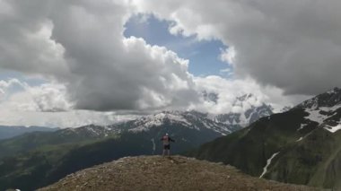 Siyahlı sırt çantalı hava aracı Svaneti 'de dağın tepesinde kollarını açıyor. Soluk kesen karlı tepeleri, yeşil vadileri seviyor. Manzarada özgürlüğü kucaklamak. Dağ yürüyüşü macerası..