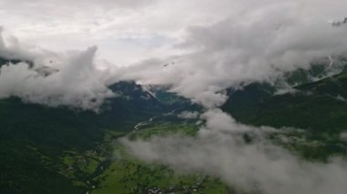 Svaneti dağlarındaki Mazeri köyünün üzerindeki bulutların hava görüntüsü. Yeşil vadiler, nehir, sis. Kırsal alan, barışçıl doğa. Puslu tepeler, manzaralı insansız hava aracı görüntüleri. Yaz mevsimi dağ manzarası.