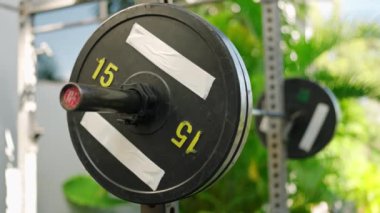 Ekipman güvenliğini sağlar, ağır kaldırma rutinine hazırlanır, sağlık ve dayanıklılık eğitimini teşvik eder. Aktif giysili kadın açık hava spor salonunda güneşli bir günde ağırlık plakasından klempi çıkartıyor..