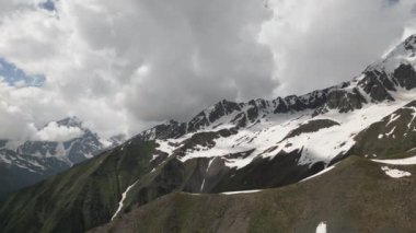 Svaneti 'deki Kafkas dağlarının, karlı tepeleri, yeşil vadileri olan hava manzarası. Sırtta yalnız bir figür. Bulutlu gökyüzü. Seyahat, macera, doğa yürüyüşü belgeseli için mükemmel bir manzara. İHA