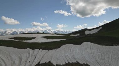 Svaneti 'deki Koruldi Dağları' nın karlı manzarası. Minivan manzaralı dağ bölgesinde off-road yapıyor. Yaz bulutları, engebeli tepeler yeşil çayırlar büyüleyici doğal bir zemin oluşturur..
