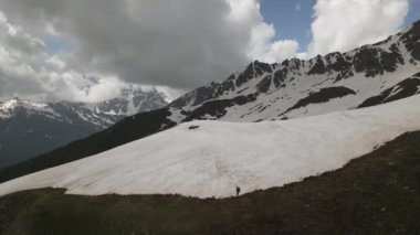 Svaneti dağlarında sırt çantasıyla inen dağcı adamın hava manzarası. Karlı tepeler, kayalık arazi, uzak bölgelerde maceralı bir yolculuk. Zorlu bir ortamda tek başına doğa yürüyüşü..