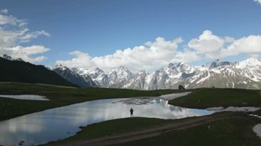 Sırt çantalı gezgin Svaneti dağlarındaki Koruldi Göllerini araştırıyor. Göl ve karlı tepelerin yanında insanın havadan görünüşü. Georgia 'da gezintiye çıkan maceraperest. Vahşi doğanın etkisi, uzak seyahat noktası..