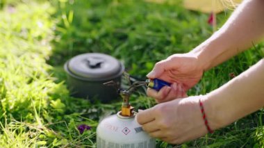 Kadın, kamp alanında taşınabilir mini gaz sobasını çakmakla tutuşturuyor. Su kaynatmak için tencereyi küçük ocağa yerleştiriyor. Açık hava gezisi için çok hafif bir sırt çantası. Kamp yapmak için mükemmel. Yavaşla