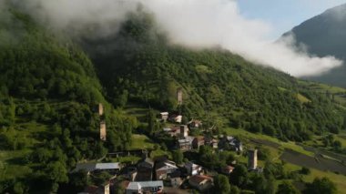 Gün doğumunda dağ vadisindeki Svan kulelerinin hava görüntüsü. Yeşil manzaradaki tarihi savunma kuleleri. Geleneksel evleri olan köy. Bulutla kaplı tepeler, etrafını saran ormanlar. Huzurlu sabah sahnesi.