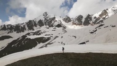 Sırt çantalı bir adam Svaneti dağlarında yürüyüş yapıyor. Karla kaplı tepeler, engebeli arazi. Tek başına gezen keşfeder, irtifa yoluna tırmanır. Macera, yürüyüş, doğa, vahşi doğa, erkeklerin kabul törenine meydan okuma..