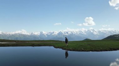 Sırt çantalı bir yürüyüşçü Svaneti dağlarında Koruldi göllerinde yürüyor. Manzaralı dağ manzarasını keşfeden maceraperest bir gezgin. Bulutların yansıması, sakin göl suyu. İHA atışı