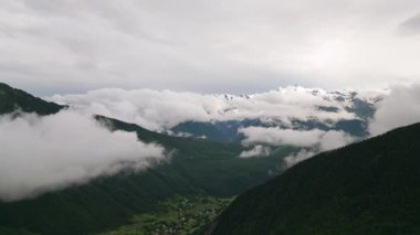 Mazeri köyü Svaneti 'deki sisli dağların hava manzarası. Yeşil vadilerin üzerindeki bulutlu gökyüzü. Manzaralı doğa, yükselen zirveler, bulutların arasında sergilenen kırsal manzara huzur dolu bir ortam. İHA atışı