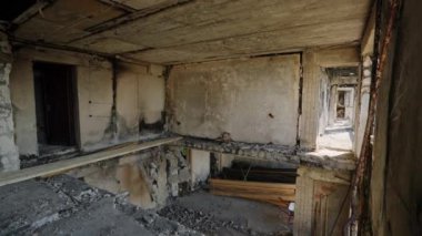 Adam apartmandaki molozların arasında yürüyor. Yanmış apartman dairesi savaş hasarı, çökmüş tavanlar gösteriyor. Şehir yıkımının gerçekçi tasviri, yeniden inşa çabaları. Video faciası sonrası.