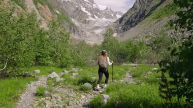 Genç bir kadın Svaneti dağlarında Chalaadi buzulunda yürüyüş yapıyor. Sırt çantasıyla kayalık patikada yürüyor, sırıkla yürüyor. Yeşil orman, karlı tepeler manzaralı manzaralar yaratır. Güneşli bir açık hava macerası. Slomo