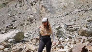 Kayalık dağ arazisinde yürüyüş yapan genç bir kadın, fotoğraflar. Kadın yürüyüşçü doğayı, dağ manzarasını telefon kamerasıyla inceliyor. Açık hava macerası manzaralı fotoğrafçılık vahşi doğada. Yavaş çekim.