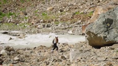 Maceracı kadın nehir kenarındaki dağlarda yürüyüş yapar. Sırt çantası, yürüyüş direkleri taşır, kayalık arazide gezinir. Doğada gündüz, büyük kayaların aktığı sularla çevrili. Vahşi doğayı keşfediyorum..