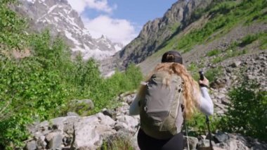 Svaneti 'deki Chalaadi buzuluna yürüyüş yapan bir kadın. Sırt çantalı bir bayan yürüyüşçü ulusal parkta kayalık yolda yürüyor. Dağlarda yürüyüş yapmak, doğa maceralarını keşfetmek. Yavaş çekim.