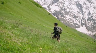 Sırt çantalı kadın Svaneti dağlarına tırmanıyor. Yürüyüşçüler yeşil çayırlarda, arka planda karlı zirveler. Güçlü bir kadın maceracı doğayı keşfeder. Açık havada seyahat, yürüyüş, doğa turizmi dağ tırmanışı..