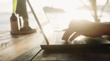 Uzaktan çalışan e- posta gönderir, projeyi tamamlar. Sahildeki kafede dizüstü bilgisayarda oturan bir adam. Freelancer teslim tarihini karşılıyor, deniz manzarası ile ilgili içerik yaratıyor. Dijital göçebe yaşam tarzı, iş hayatı dengesi..