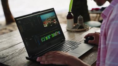 Freelancer deniz yoluyla yaratıcı içeriği düzenliyor. Video editörü, plaj kafede dizüstü bilgisayarda çalışıyor. Gün batımında ise renk derecelendirme filmlerinde. PC ekranında çeşitli proje zaman çizgileri açılıyor. Manzaralı açık hava ortamında uzak çalışma.