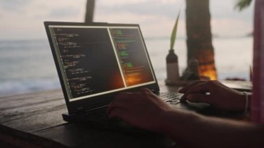 Erkek programcı kod yazıyor. Palmiye ağaçlarının yakınında çalışıyor. Altın saat boyunca deniz dalgaları. Sahil kenarındaki kafede dizüstü bilgisayarda yazılım geliştiren tipler, okyanus batımı arkaplanı. Serbest İşçi Projesi Sahili.