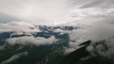 Svaneti 'deki Mazeri köyü dağlarının hava manzarası. Bulutlar sürükleniyor. Yeşiller yemyeşil ormanlar, bulutlarla kontrastlı tepeler. Sakin doğa manzarası uzak dağ manzarası. İHA atışı