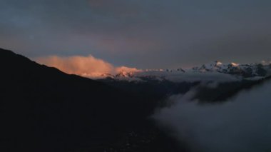 Svaneti dağlarındaki Mazeri köyünün üzerinde gün batımı. Güneş ışığı vadideki karlı tepelere vurur. Alacakaranlıkta dağ siluetiyle huzurlu kırsal manzara. Göz kamaştırıcı doğal manzara. İHA atışı
