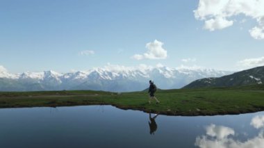 Sırt çantalı bir yürüyüşçü Svaneti dağlarında Koruldi göllerinde yürüyor. Doğayı keşfeden yalnız gezgin, suya yansıyan alp manzarası. Macera seyahati, Georgia 'da doğa yürüyüşü..