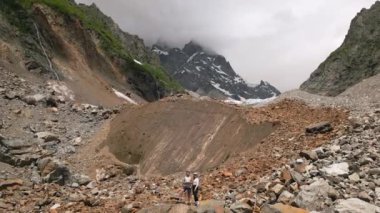 Svaneti dağlarında yürüyüş yapan kadının hava görüntüsü. Buzulları, şelaleleri ve engebeli yamaçları olan kayalık alp arazisi. Açık hava macerası, doğa keşfi, yürüyüş, dağ yürüyüşü, açık hava sporları. İHA