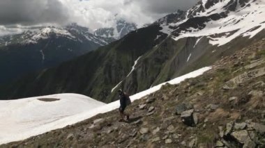 Karla kaplı zirveleri olan yüksek dağlarda tek başına yürüyüş yapan biri. Adam sırt çantasıyla kayalık arazide yürüyor. Vahşi doğada kış macerası. Seyahat, keşif, uzak patika.