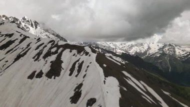 Karla kaplı tepeleri ve bulutlu gökyüzü olan Svaneti dağlarının hava manzarası. Heybetli manzara engebeli araziyi, yüksek irtifayı gösteriyor. Manzaralı kış ortamı. Dağlar, kar bulutları ve kayalar. İHA