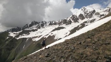 Solo dağcı sırt çantasıyla karlı dağa tırmanıyor. İnsanoğlunun yüksek dağlarda dik kayalık yamaçlara yükselişinin havadan görünüşü. Açık hava macerası, ekstrem spor, manzara gezisi turizmi. İHA atışı