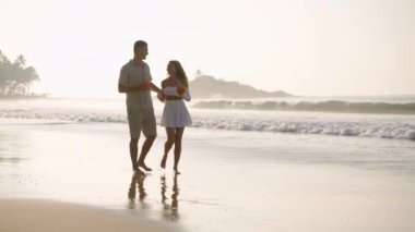 Neşeli çift deniz sörfünün kenarında hindistan cevizi kokteyli içiyor. Gençler gün batımında okyanus kıyısında el ele tutuşmaktan bahseder. Gezginler tropikal adada romantik bir gezide eğleniyorlar..