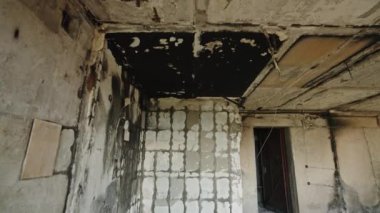 Yanmış duvarlar, açıkta kalan kirişler ve enkaz ıssız uzayı sarar. Yanmış, savaştan zarar görmüş, çökmüş tavanlı bir apartman dairesi..