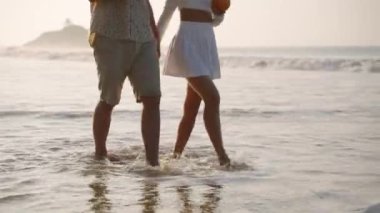 Romantik bir adam, deniz sörfünde el ele yürüyen bir kadın. Güzel bir çift gün batımında okyanus kıyısında rahatlayacak. Erkek arkadaş, kız arkadaş hindistan cevizi kokteyli içer, kumsalda buluşmanın tadını çıkarır..