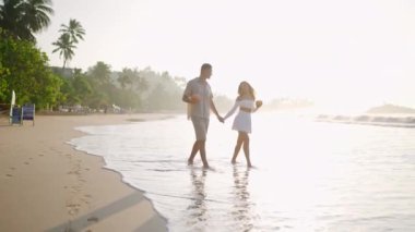 Aşık bir kadın deniz kenarında yalınayak yürür. Islak kumsalda hindistan cevizi kokteyli içen çiftin yansıması. Okyanus kıyısı dalgalarına giden insanların gölgesi. Sevgililer tatilde el ele tutuşur.