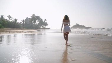 Tropik adada deniz sörfünde çıplak ayakla yürüyen bir buket çiçekli çekici bir model. Romantik kız okyanus kıyısında rahatlıyor. Genç bir kadın kumsalda yaz tatilinin tadını çıkarıyor..