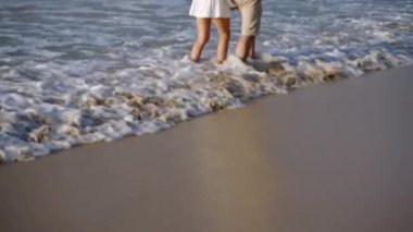 Erkek arkadaş, kız arkadaş deniz dalgalarında yalın ayak yürüyor, su sıçratıyor. Genç çift okyanus kıyısında el ele tutuşarak konuşuyor. Romantik gezginler tropik ada sahillerinde dinleniyor.