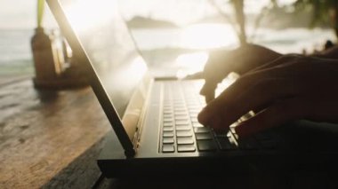 Okyanus üzerinde güneş ışığı parlıyor, uzak çalışma ortamı, dijital göçebe yaşam, deniz kenarında verimli bir ortam. Adam gün batımında bilgisayarda çalışıyor, plaj kafesinde, klavyede daktilo yazıyor, serbest yaşam tarzı konsepti. Yavaşla