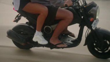 Şık bir çift gün doğumunda deniz sahilinde motosiklet sürüyor. Bisikletten insana aktarma kurulumu. Turistler okyanus kıyısında kiralık motosiklet kullanıyorlar. Kadınlar erkeklere sarılır, motosiklet sürerken kollarını açar..
