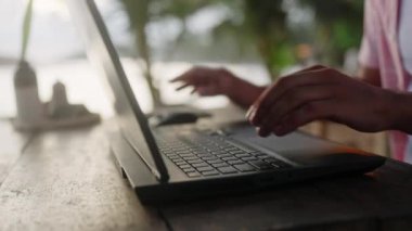 Uzaktan çalışma konsepti, serbest yaşam tarzı. Sunset Beach Cafe 'de dizüstü bilgisayarda yazan bir adam. Eller klavye tuşlarına basar, dijital göçebe tipler okyanus kenarında güzel bir alacakaranlıkta. İş seyahati, rahat çevre.