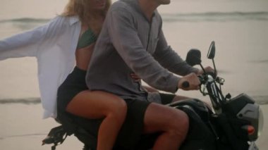Şık bir çift gün doğumunda deniz sahilinde motosiklet sürüyor. Bisikletten insana aktarma kurulumu. Turistler okyanus kıyısında kiralık motosiklet kullanıyorlar. Kadınlar erkeklere sarılır, motosiklet sürerken kollarını açar..