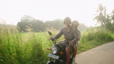 Motosikletle seyahat eden neşeli genç bir çift. İki neşeli aşık orman yolunda motosiklet sürüyor. Kız arkadaşı gülümsüyor, erkek arkadaşına sarılıyor. Gezginler gün batımında scooter kullanır. Erkek, kadın scooter macerası.