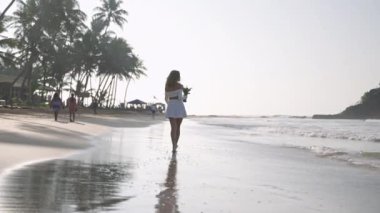 Tropik adada deniz sörfünde çıplak ayakla yürüyen bir buket çiçekli çekici bir model. Romantik kız okyanus kıyısında rahatlıyor. Genç bir kadın kumsalda yaz tatilinin tadını çıkarıyor..