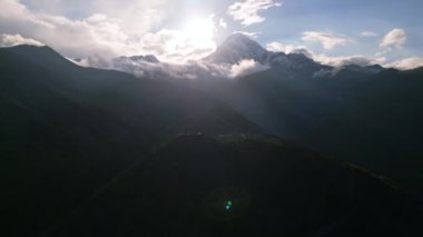 Kafkasya dağlarındaki Gergeti Trinity Kilisesi 'nin bulutlarla, güneşle çevrili Kazbegi tepesinin havadan görünüşü. Gürcistan 'ın güzel manzarası, seyahat ve turizm macerası için mükemmel. İHA atışı