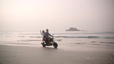 Romantik çift gün doğumunda deniz sahilinde motosiklet sürüyor. Kadınlar, tropik adalarda okyanus boyunca motorsikletle seyahat ederler. Kız sevgilisine sarılıyor. Motivasyon arkaplanı.