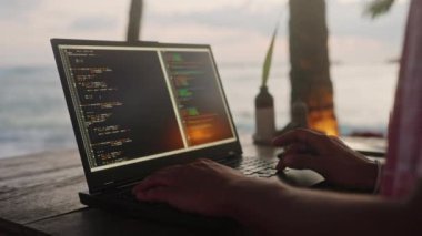 Erkek yazılım kodlayıcısı, palmiyeler ve deniz ortasındaki proje için kod oluşturur. Sahil Kafe 'de dizüstü bilgisayarda günbatımı okyanus üzerinde olan web geliştiricileri. Uzaktan çalışma konsepti eğlence ve profesyonel görevleri birleştirir. Yavaş çekim.