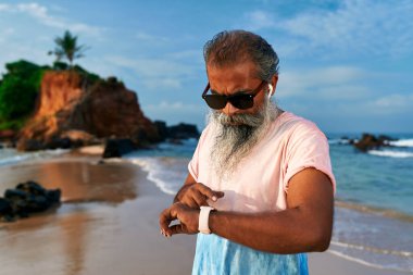 Son sınıf öğrencisi, kumsalda akıllı saat kullanır. Güneş gözlüğü takıyor. Modern büyükbaba okyanus manzarasını sever. Fitness izleyicili aktif bir yaşam tarzı. Aygıtları bağlar.