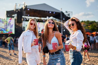 Grup, yaz etkinliğinin, kumlu sahil sahnesinin keyfini çıkarıyor. Moda kıyafetleri plaj müzik festivalinde pembe içkileri kutluyor. Arkadaşlık anları, arka planda eğlenceli kutlama kalabalığı. Günlük yaşam tarzı, açık hava..